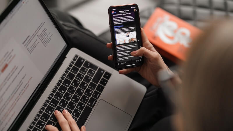 Woman scrolling through phone while on laptop