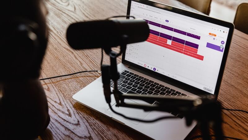 A microphone on an arm in front of an open laptop showing recording software